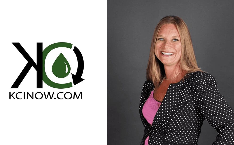 Professional woman smiling, standing against a gray background with a logo on the left.