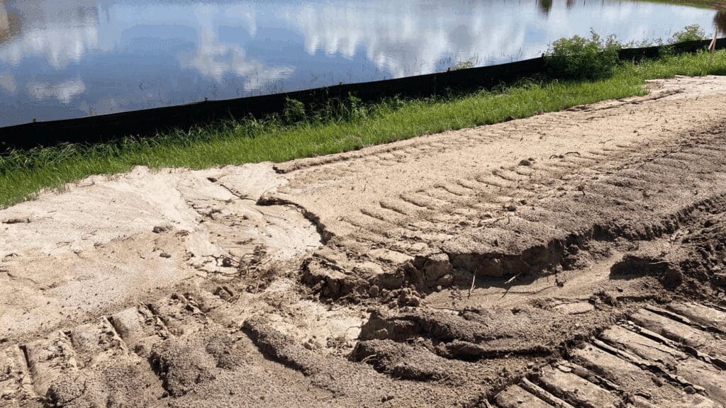Fresh tire tracks on a sandy path near a water body.