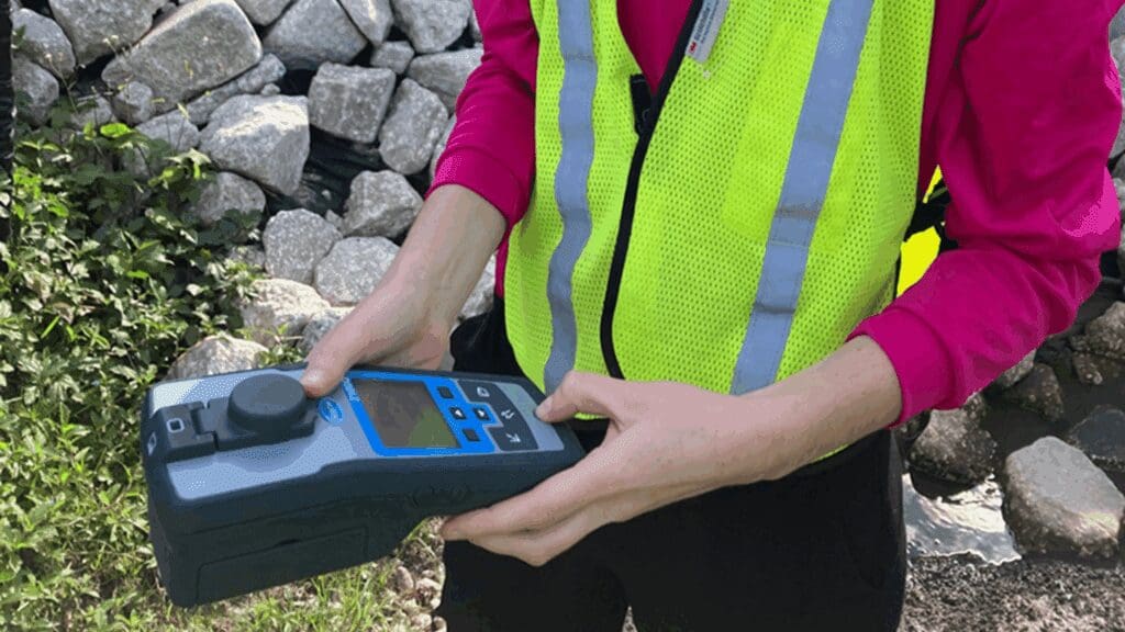 Person operating a handheld device near rocks, wearing a reflective safety vest.
