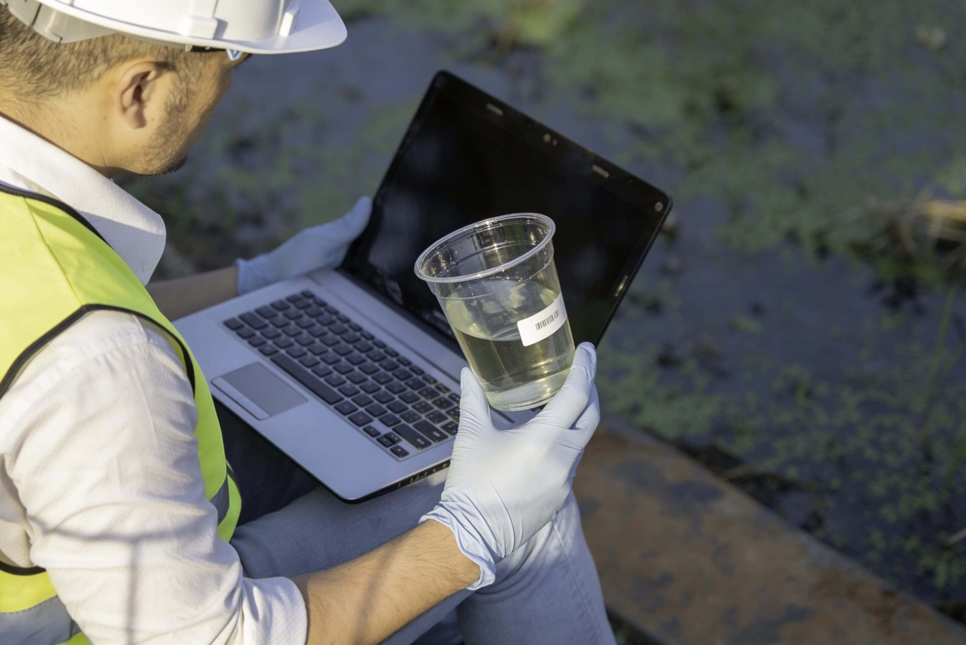 A person holding a glass of water in front of a laptop outdoors.