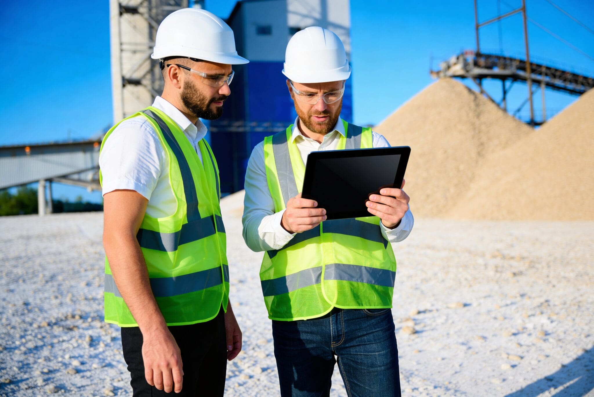 Two construction workers reviewing plans on a tablet at a site.
