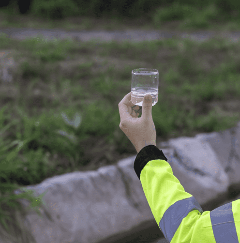A person in a yellow jacket holding a clear plastic cup with water.