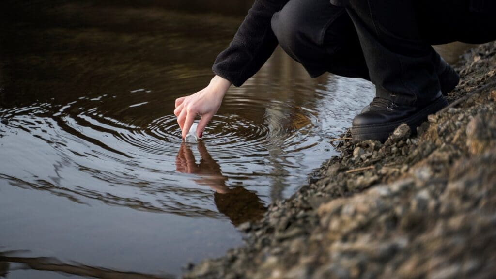 Person's hand touching water surface near rocky shore.