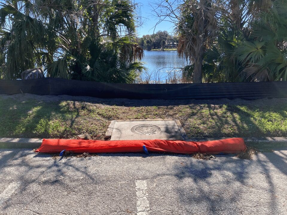 A fallen tree blocks a paved trail near a pond in a park.