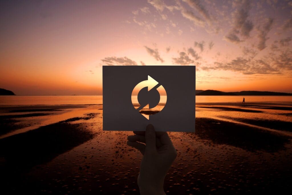 Hand holding a card with a recycle symbol against a sunset at the beach.