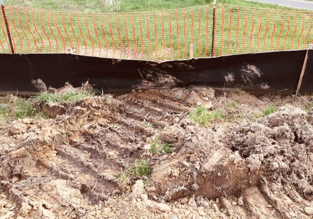 Fresh tire tracks on muddy soil near a grassy field.
