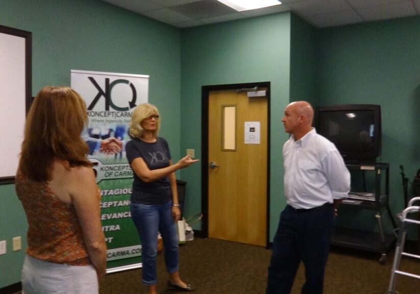 Three people engaged in a discussion in an office room with a banner.
