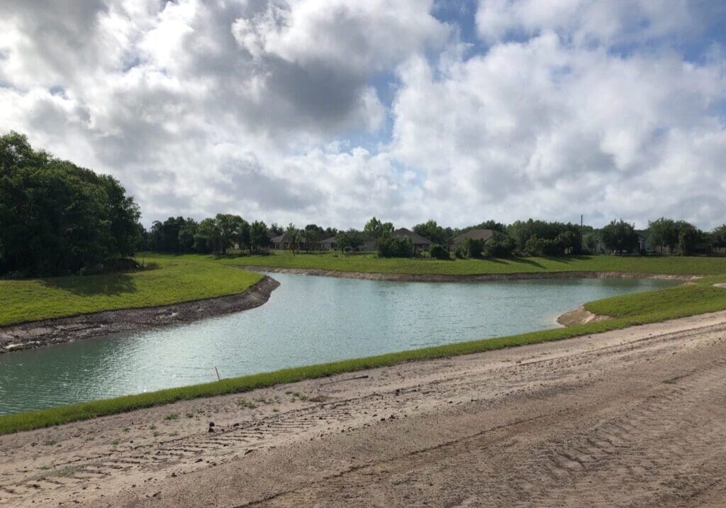 A calm river flows under a cloudy sky beside a dirt path.