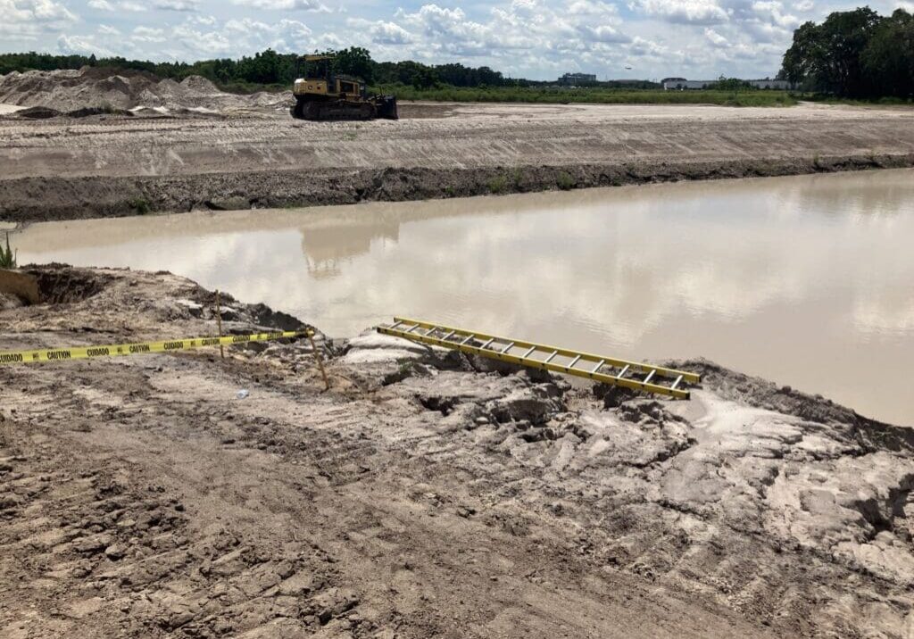 A muddy construction site with a large puddle and machinery in the distance.