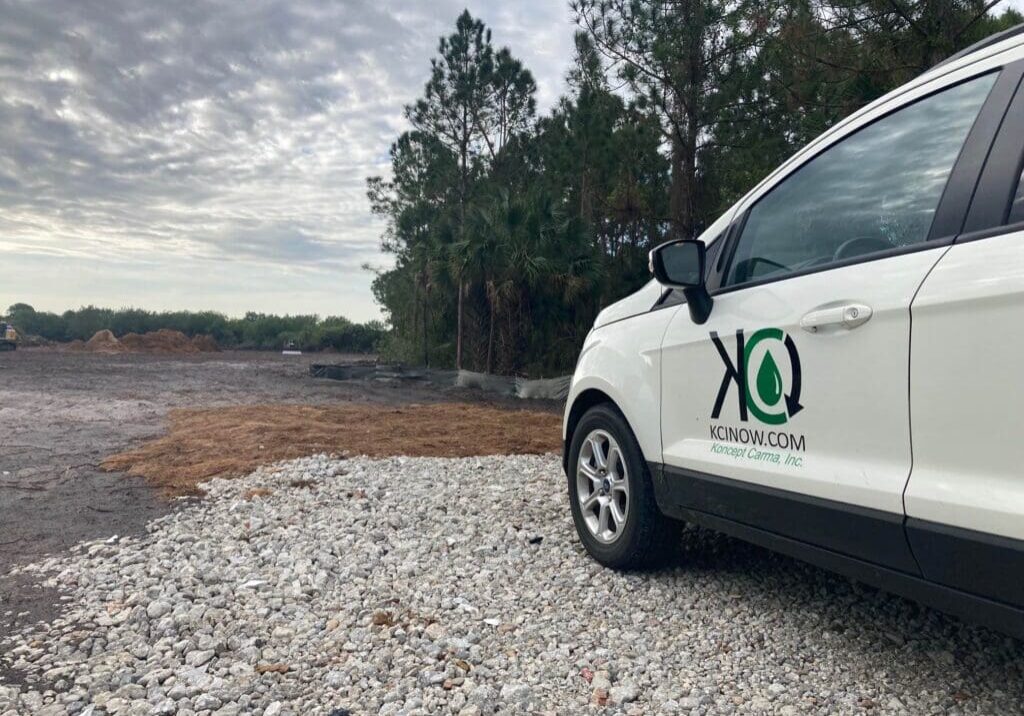 A white vehicle with a logo parked on a gravel road near trees under a cloudy sky.