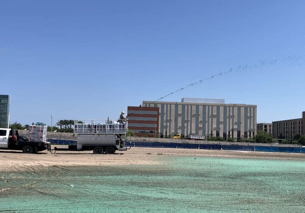 Clear turquoise water in front of a sandy beach with buildings under a bright blue sky.