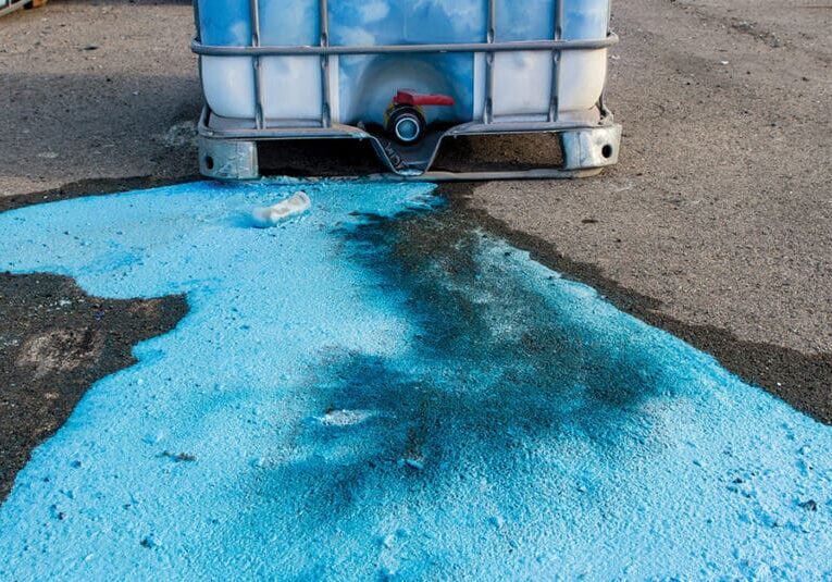 Blue liquid spills from a container onto the ground.