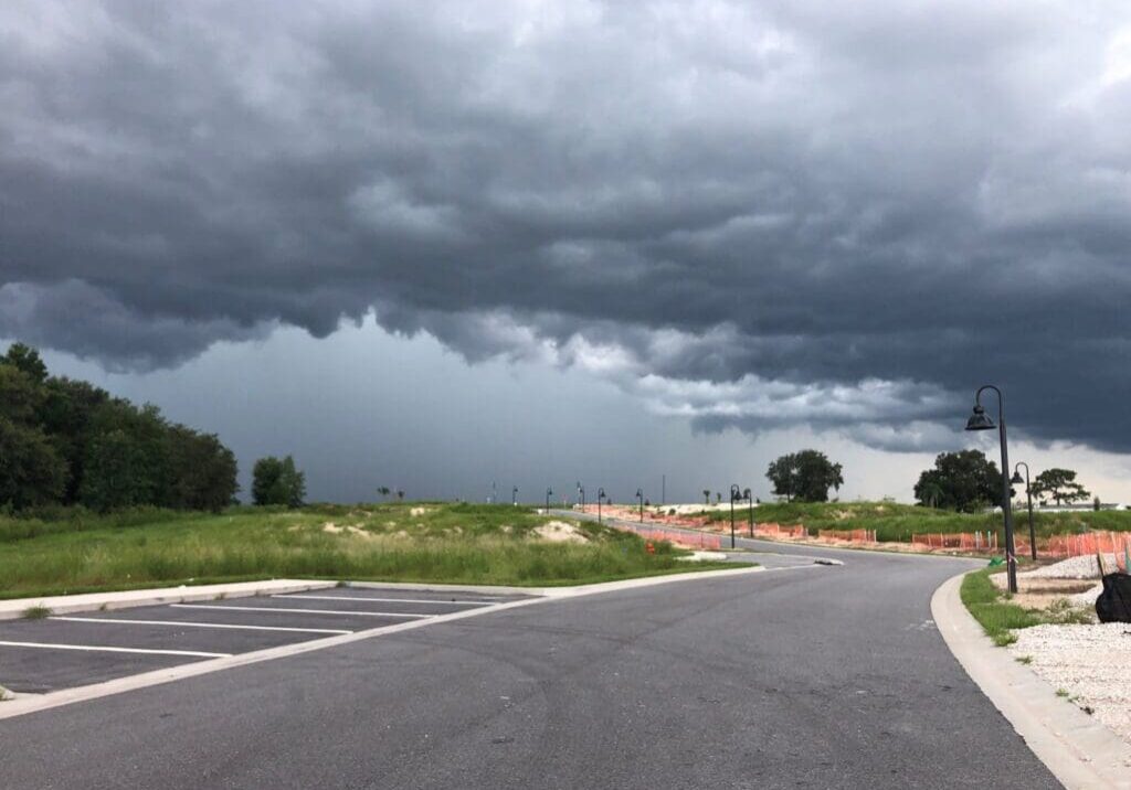 Dark storm clouds gather over an empty road and grassy fields.