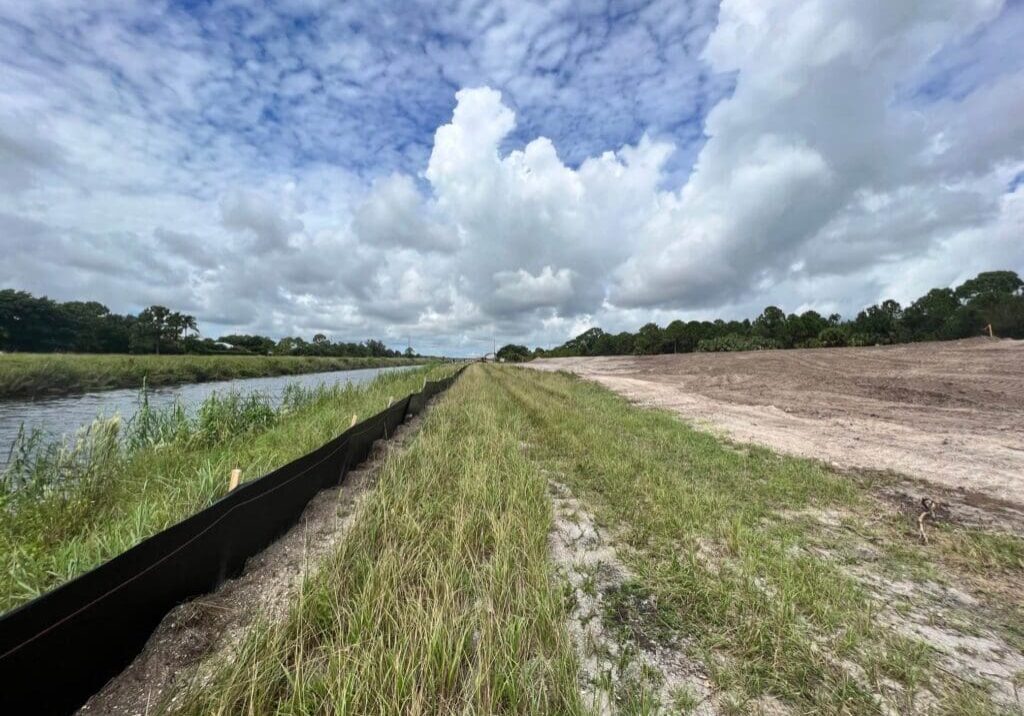 A scenic grassy path beside a calm waterway under a partly cloudy sky.