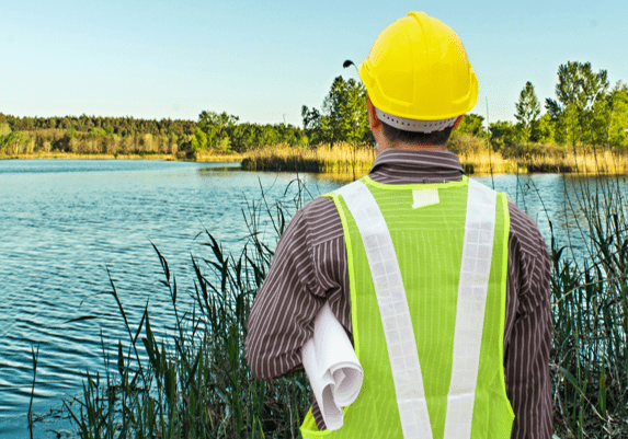 Engineer in safety gear inspecting a water body outdoors.