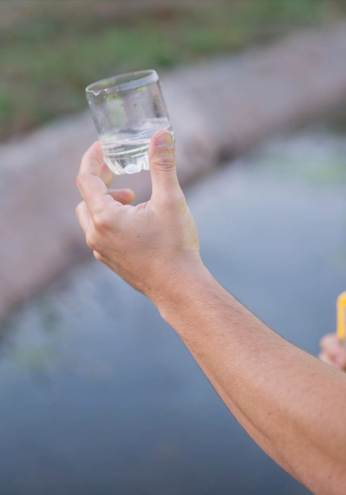 Person holding a glass of clear water near a pond.