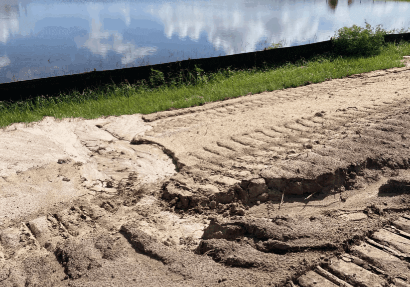 Fresh tire tracks on a sandy path near a water body.