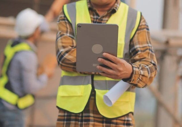 Worker in a safety vest holding a tablet on a construction site.