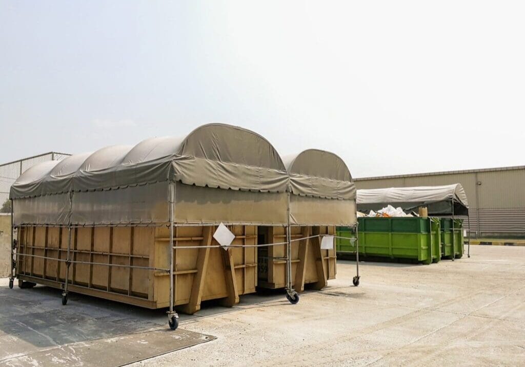 Two covered outdoor structures with barrels underneath on a concrete surface.