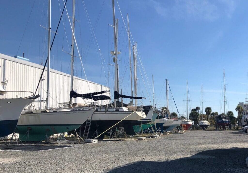 Several sailboats docked on land beside a warehouse under a clear blue sky.