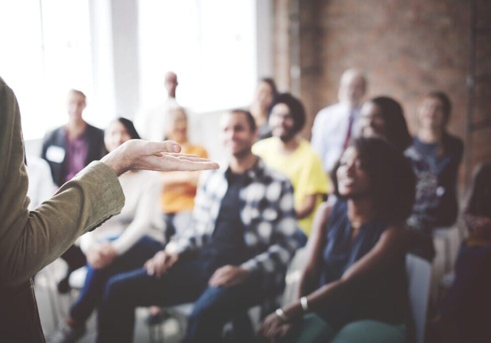 A person giving a presentation to an engaged audience in a bright room.