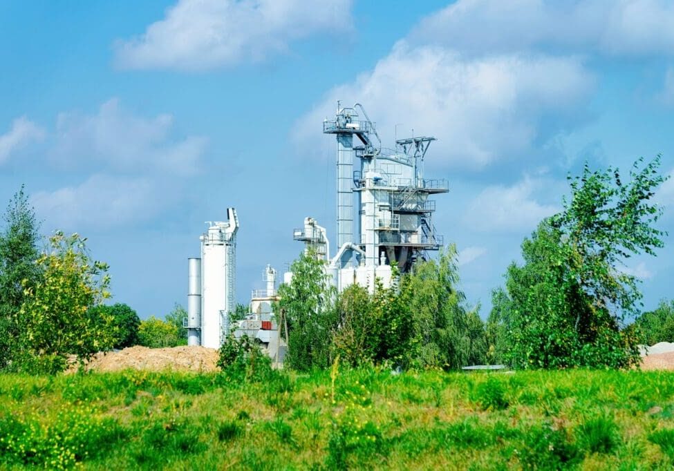Industrial plant with tall structures amidst greenery under a blue sky.