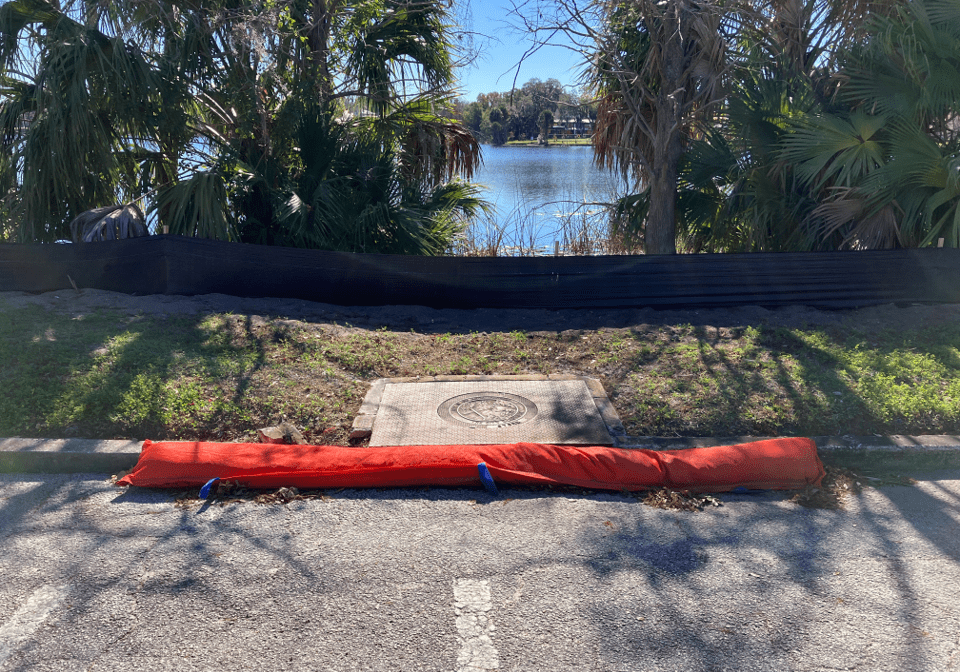 A fallen tree blocks a paved trail near a pond in a park.