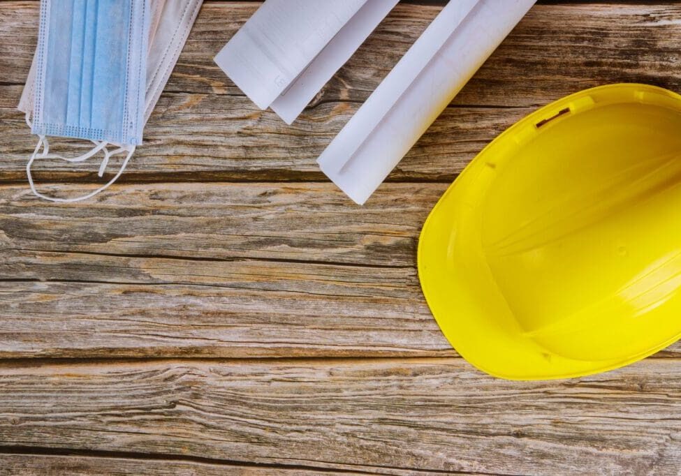 Yellow hard hat and blueprints on a wooden table.