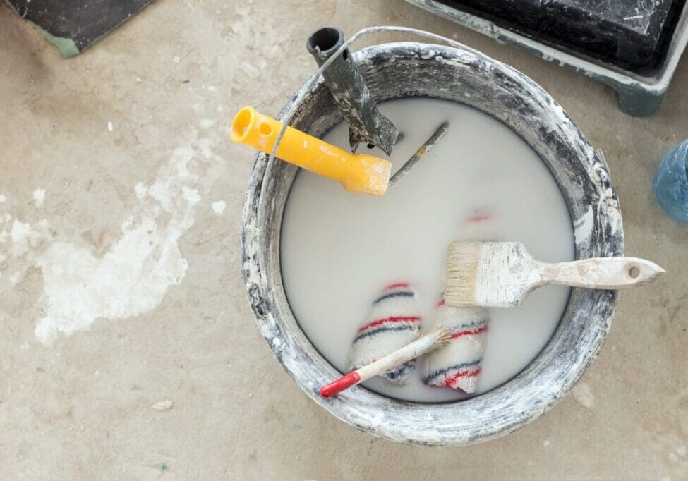 Paint bucket with white paint and a brush resting inside.