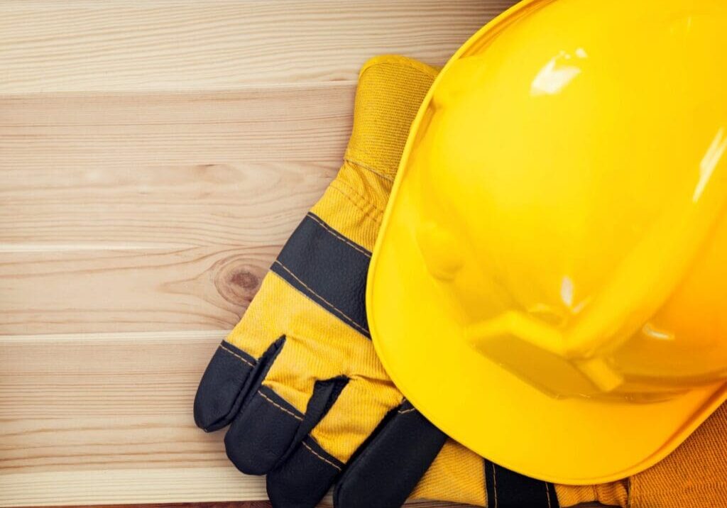 Yellow safety helmet and gloves on wooden surface.