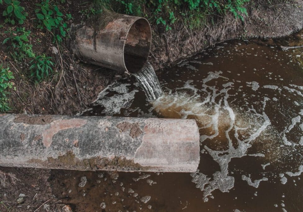 Dirty water flows from a pipe into a polluted stream.