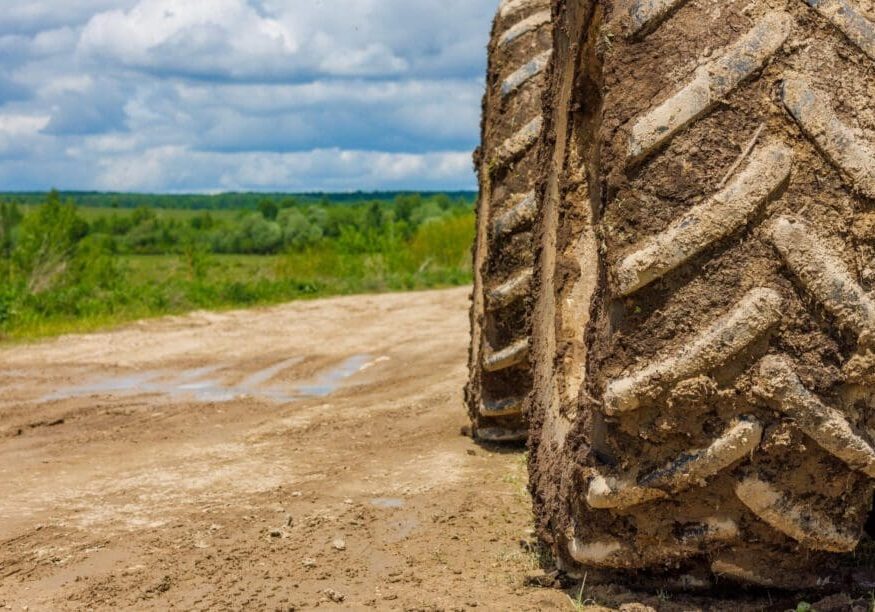 Close-up of large tractor tires on a dirt path with green fields and cloudy sky.