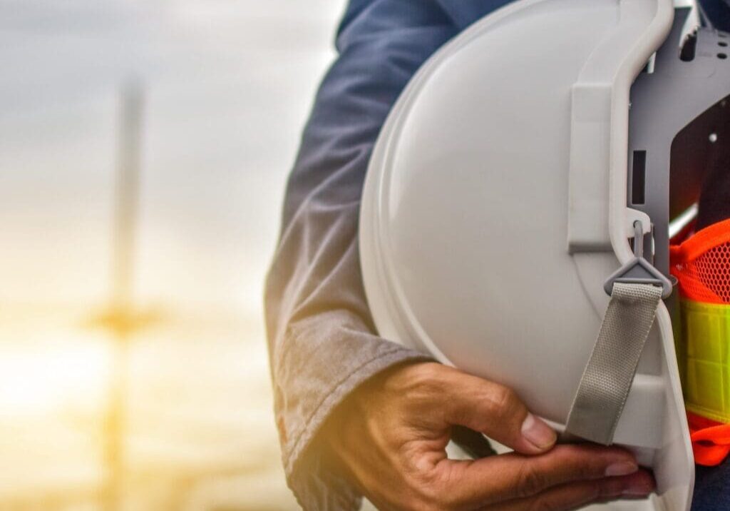 Person holding a white construction helmet at a job site during sunset.
