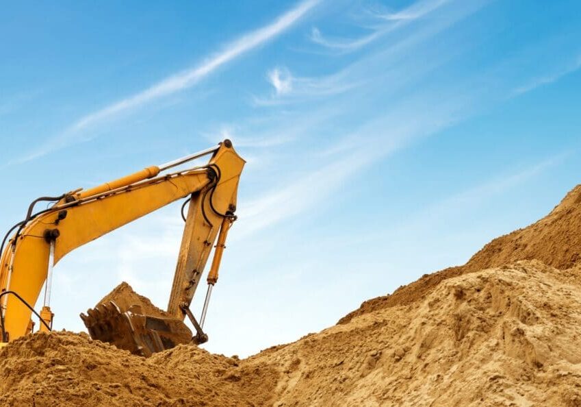 Excavator digging earth under a clear blue sky.