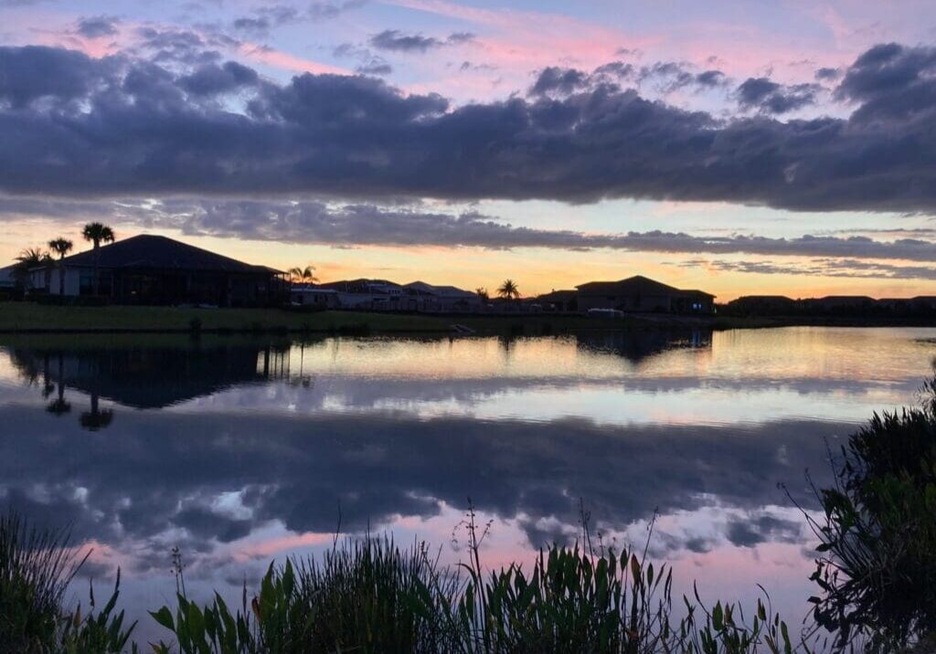 Sunset over a calm lake with silhouetted hills and a cloudy sky.