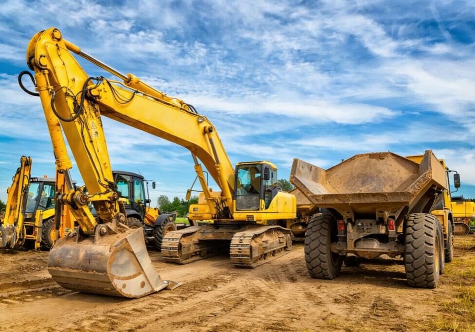 Construction vehicles working on a dirt site under a blue sky.