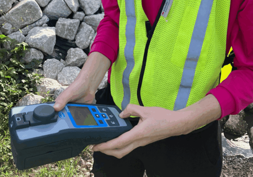 Person operating a handheld device near rocks, wearing a reflective safety vest.