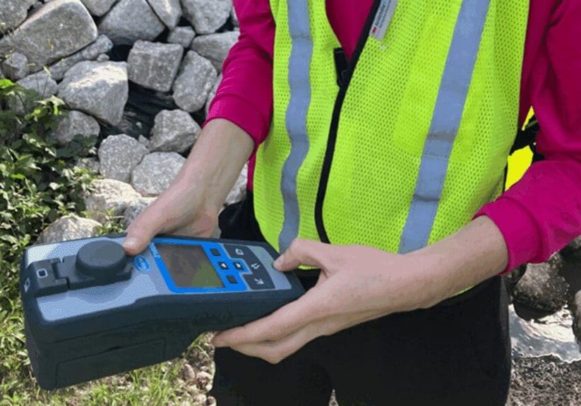 Person operating a handheld device near rocks, wearing a reflective safety vest.