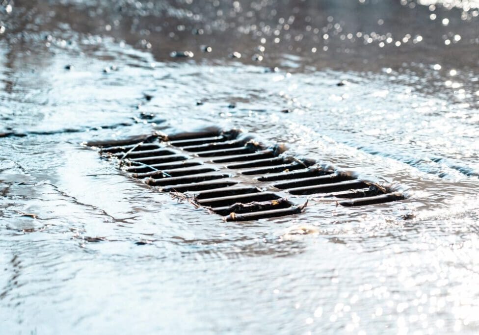 Rainwater flowing into a street drain under heavy rainfall.