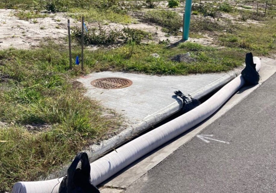 Drain cover with a pipe along a roadside, surrounded by grass.