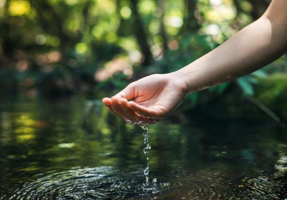 Hand gently touching clear water in a natural setting.