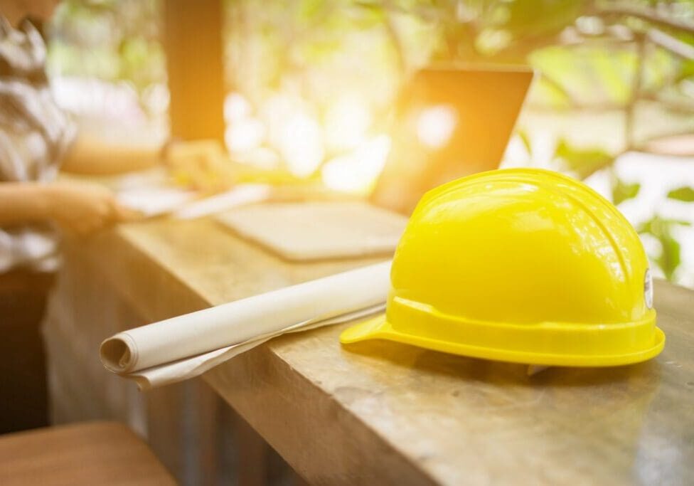 Yellow construction helmet and pen on wooden table with sunlight.
