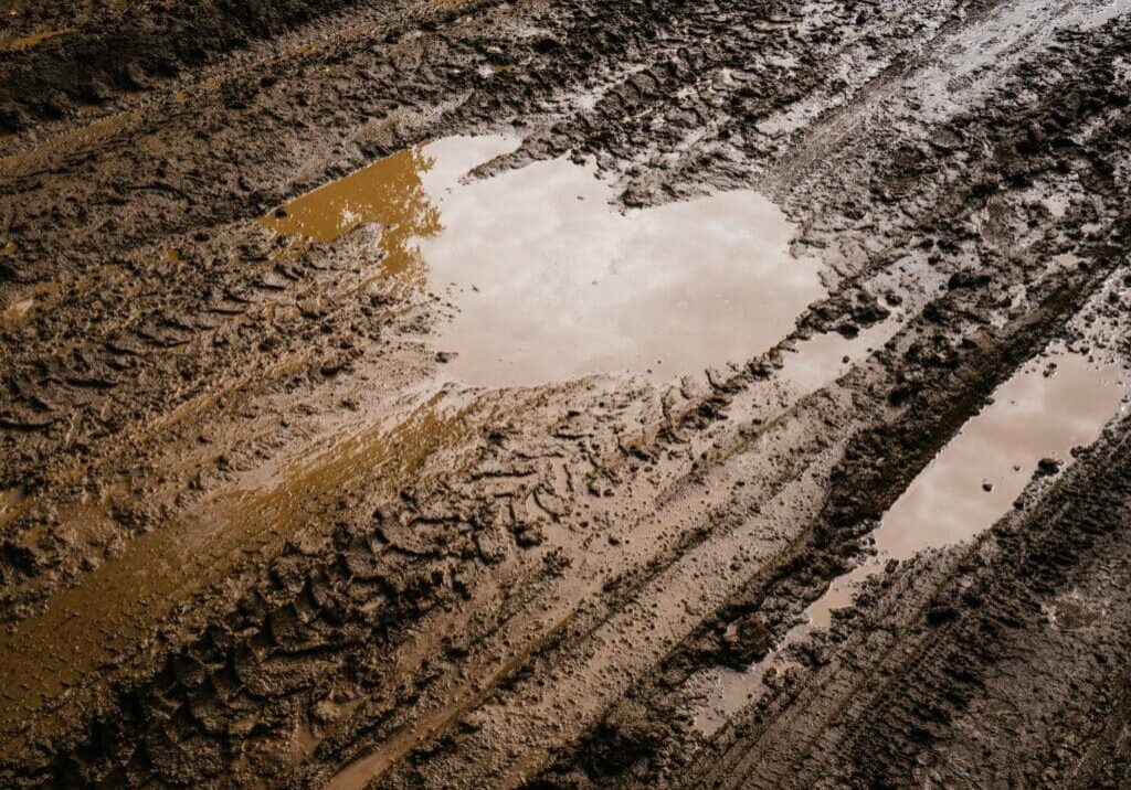 Muddy tire tracks with a heart-shaped puddle on a dirt road.