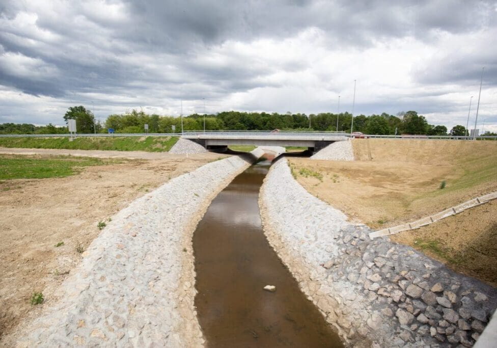 A small canal with stone-lined banks flowing under a concrete bridge.