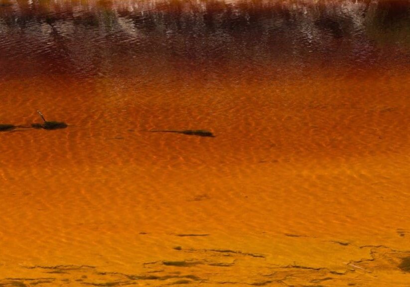 A serene lake reflecting warm orange and brown hues from the surrounding landscape.
