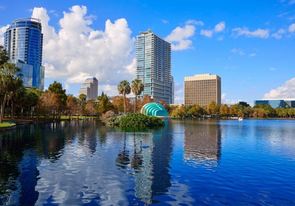 City skyline reflected in a lake with blue skies and scattered clouds.