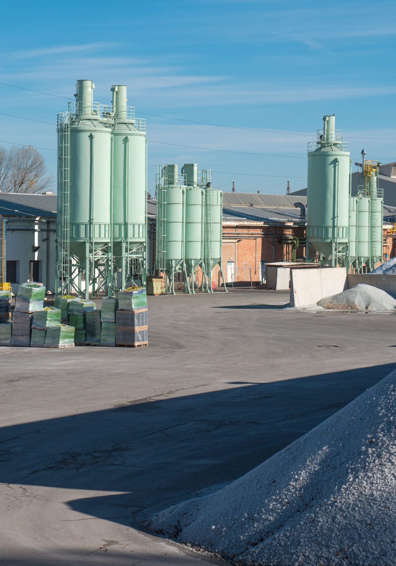 Industrial site with large storage silos and gravel piles under a clear sky.