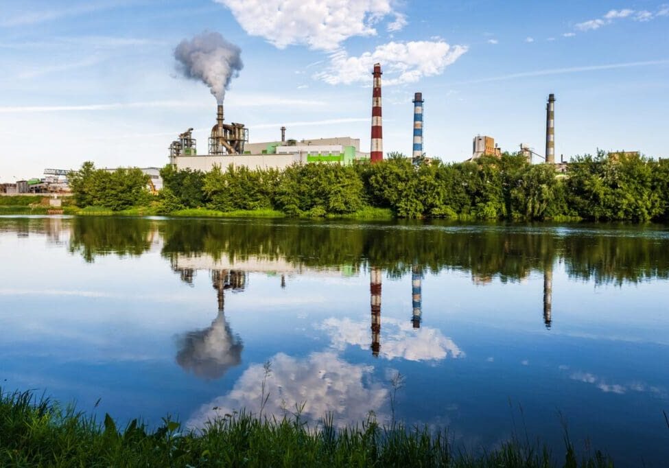 Industrial plant with smokestacks reflecting in a calm water body.