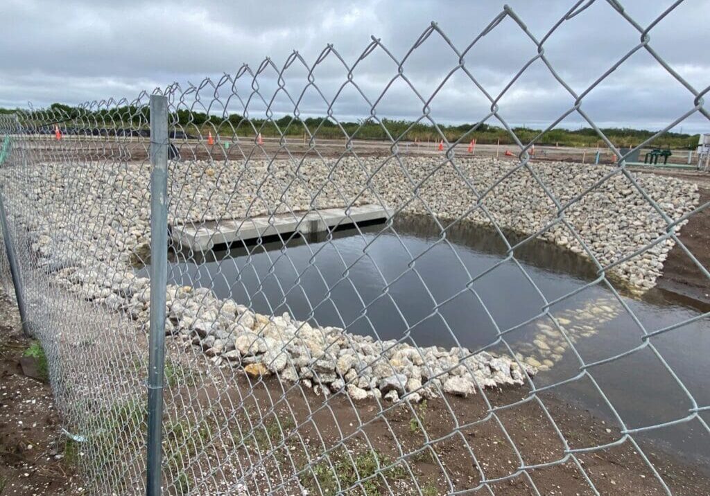 A fenced water reservoir surrounded by rocks under cloudy sky.