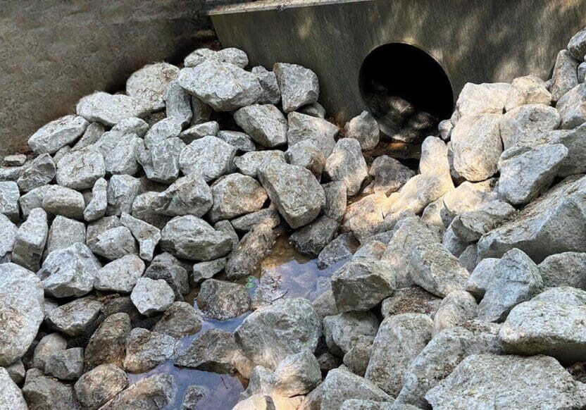 Pile of gray rocks near a black drainage pipe.